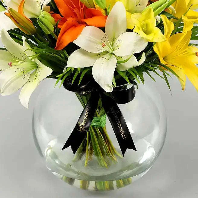 تنسيقة زهور الزنبق الملونة مع أوراق النخيل في وعاء زجاجي كروي flowerna