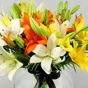 تنسيقة زهور الزنبق الملونة مع أوراق النخيل في وعاء زجاجي كروي flowerna