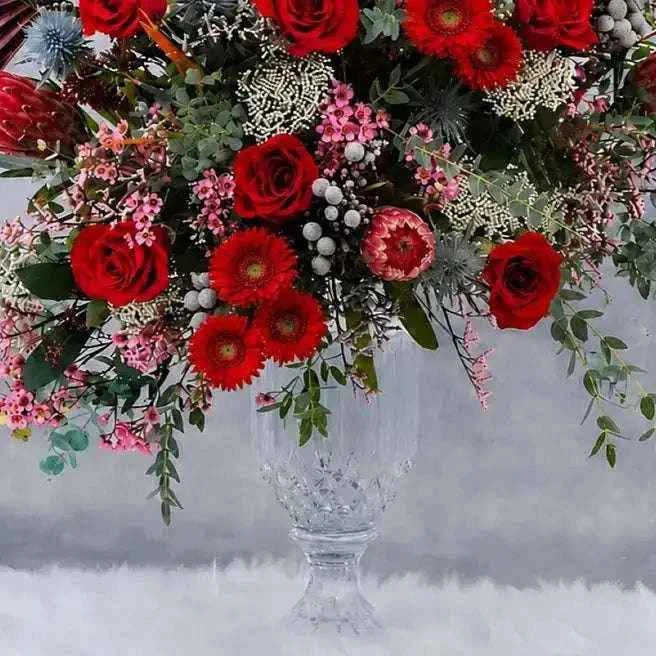 تنسيقة الزهور البرية في فازة زجاجية مع طيور الجنة والبروتيا والورد الأحمر