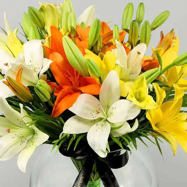 تنسيقة زهور الزنبق الملونة مع أوراق النخيل في وعاء زجاجي كروي flowerna