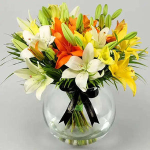 تنسيقة زهور الزنبق الملونة مع أوراق النخيل في وعاء زجاجي كروي flowerna