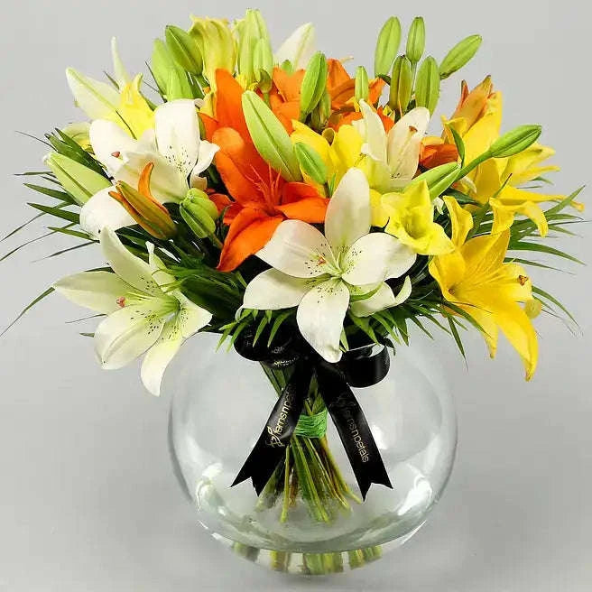 تنسيقة زهور الزنبق الملونة مع أوراق النخيل في وعاء زجاجي كروي flowerna